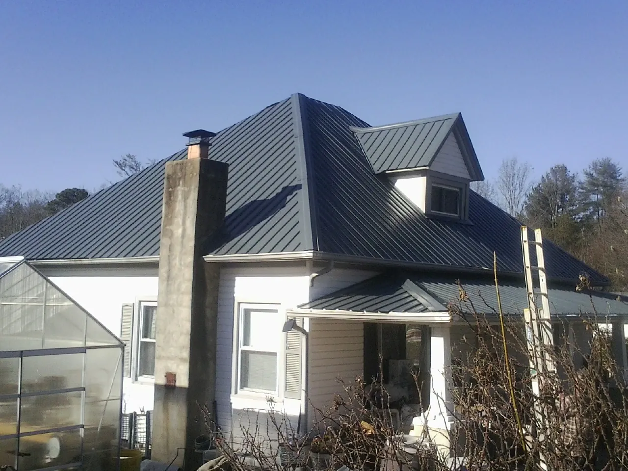 Dark blue standing seam metal roof on a white farmhouse with dormer — Slate & Tile Roof Repair by Roofing Brothers in Laughlin