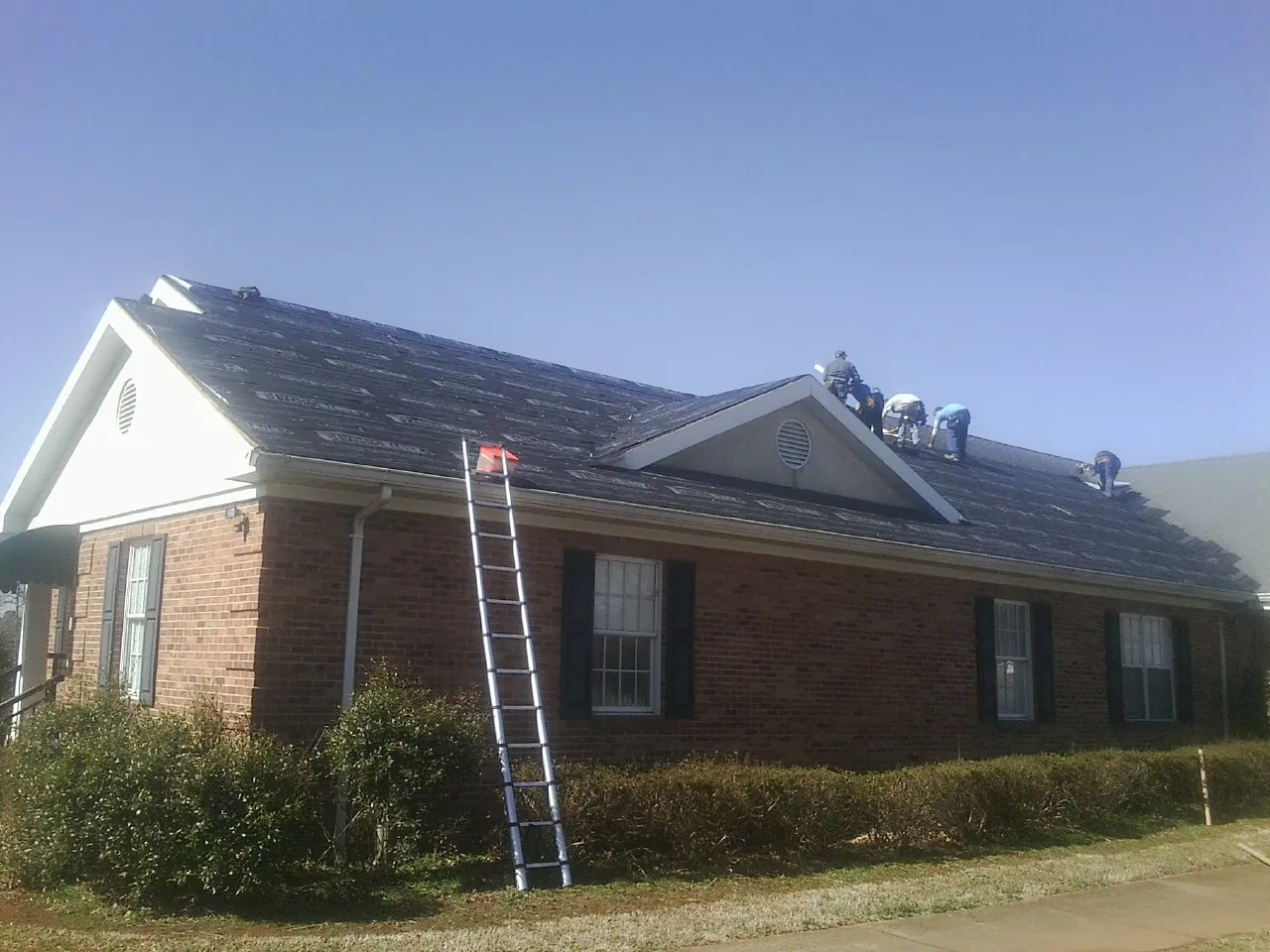 Crew tearing shingles off a brick ranch roof with a ladder set — Emergency Roof Repair work by our crew in Laughlin