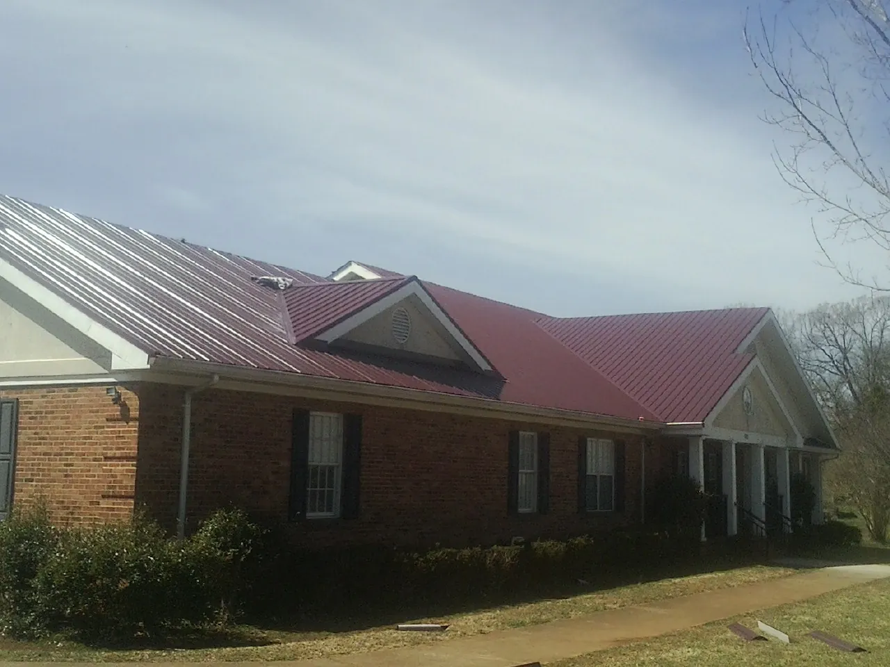 Red metal roof with gabled entries on a long brick building, from a Hail Damage Roof Repair job in Laughlin