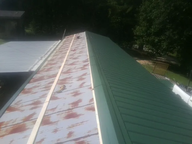 Old rusted panels beside newly installed green metal roofing — Wind Damage Roof Repair by Roofing Brothers in Laughlin