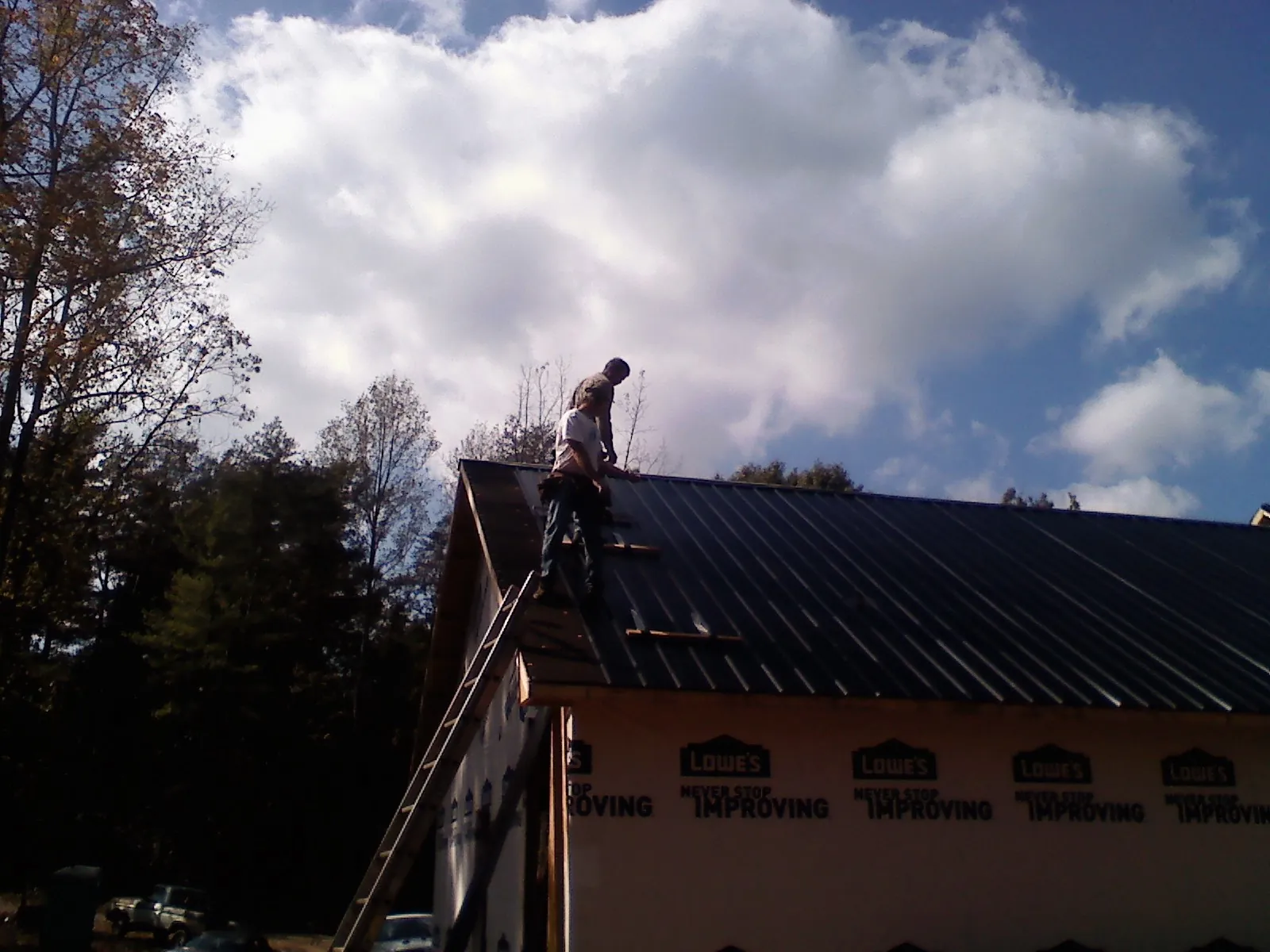 Roofer fastening dark metal panels high against a cloudy sky, from a Roof Inspection job in Laughlin